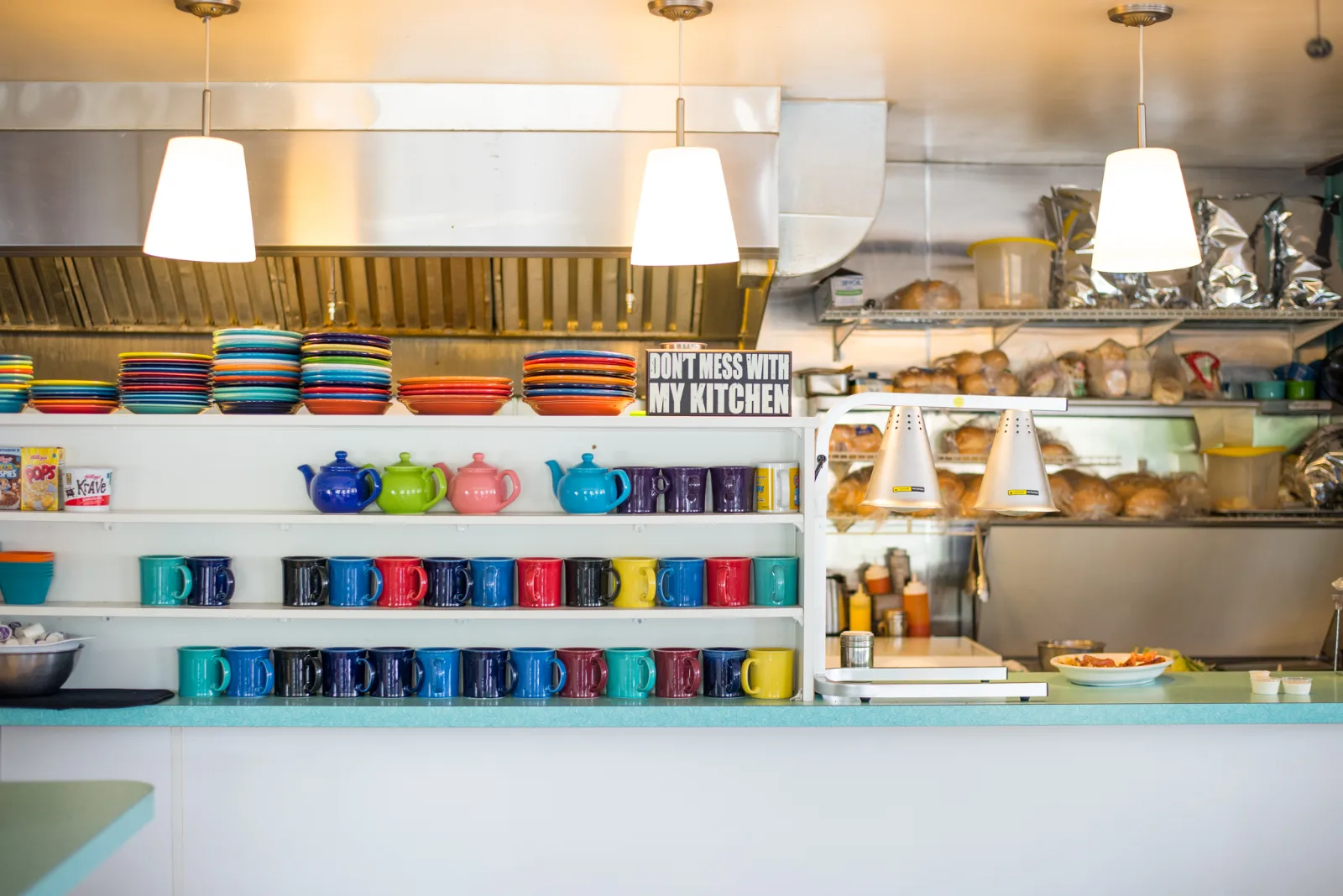 Our Diner’s counter, lined with colorful mugs, stacked plates and teapots under pendant lights